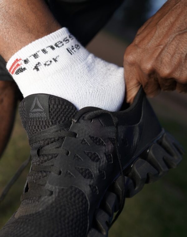 A person putting on their shoes with one foot in the air.